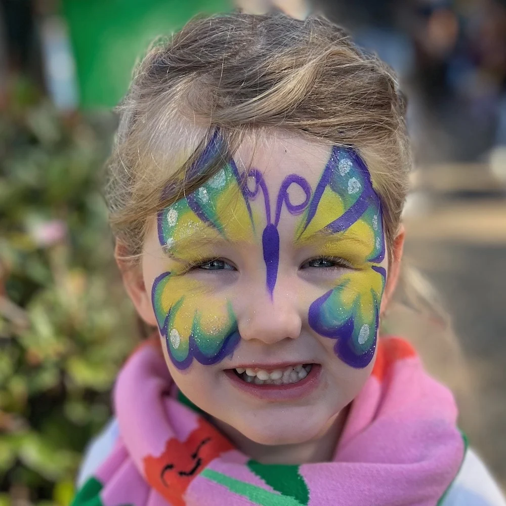 A KidzKlub face painting station at a family friendly event with a happy child with a colourful butterfly design.