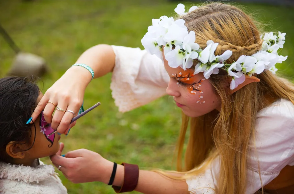 woman with flower in her hair does facepainting on young girl